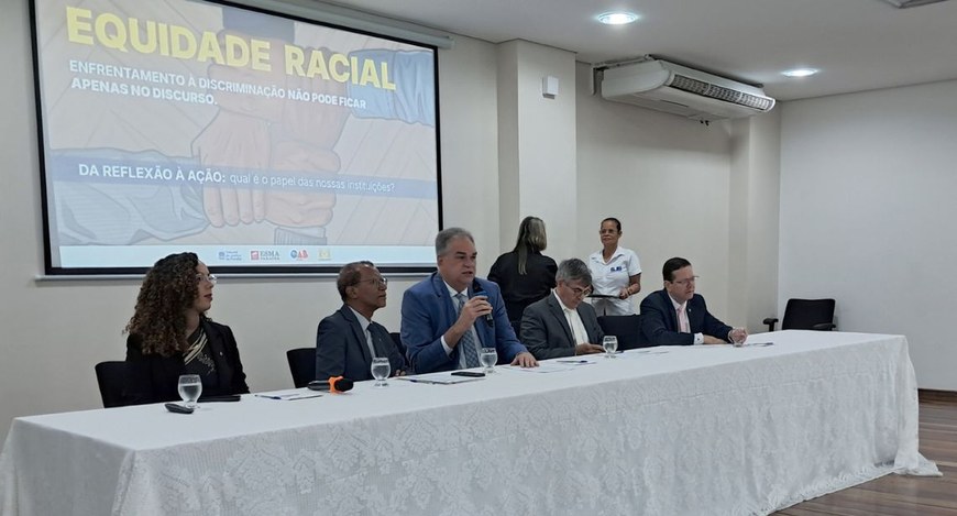 #PraTodosVerem: Na fotografia aparecem várias pessoas sentadas, diante de uma mesa retangular. A...