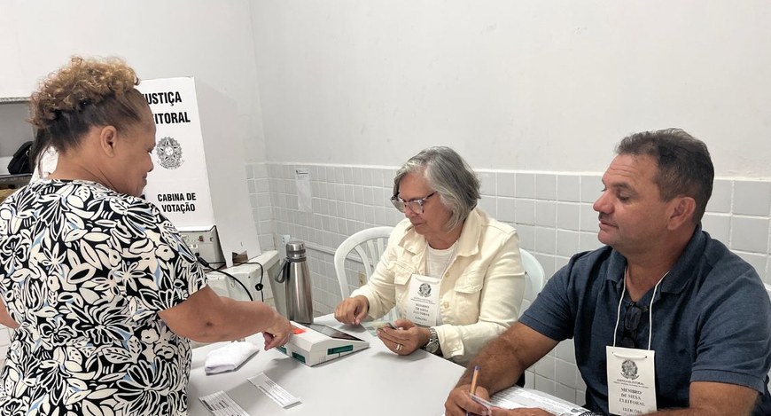 #PraTodosVerem: Na fotografia, aparecem duas pessoas sentadas, atuando como mesários voluntários...