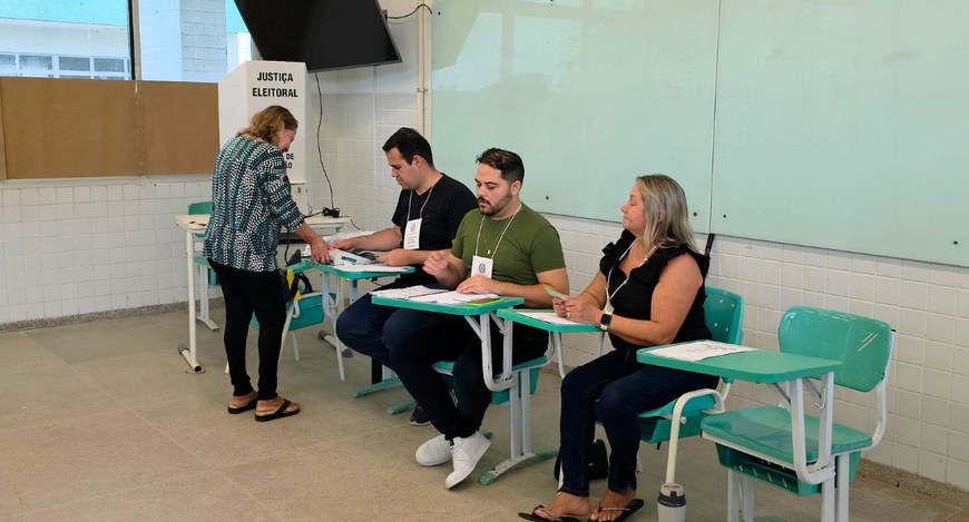 #PraTodosVerem: Na fotografia aparecem três mesários atuando numa sessão, tendo uma eleitora em ...