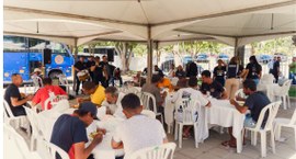 #PraTodosVerem: Na fotografia aparecem pessoas fazendo refeição em mesas de plástico embaixo de ...