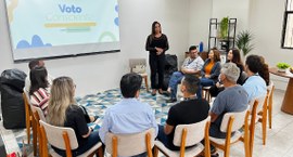TRE-PB debate voto consciente e diversidade em roda de conversa #PraTodosVerem: Na fotografia aparece uma mulher em pé, vestida de preto, conduzindo uma palestr...