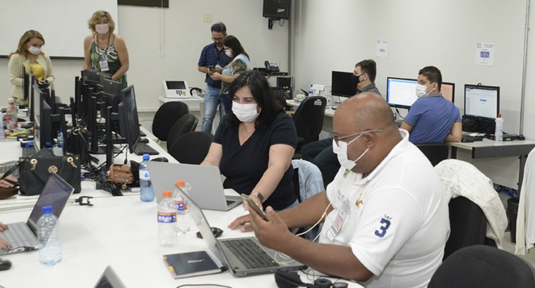 #ParaTodosVerem: Servidores e servidoras trabalhando de pé e sentados e sentadas em várias mesas...