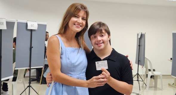 Foto 1: #PraTodosVerem: Na fotografia aparece uma mulher de vestido azul claro abraçada a um jov...