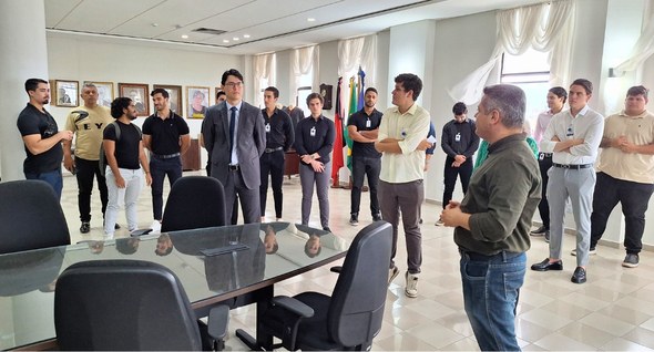 #PraTodosVerem: Na fotografia aparece um grupo pessoas em uma sala ampla, com paredes brancas, j...