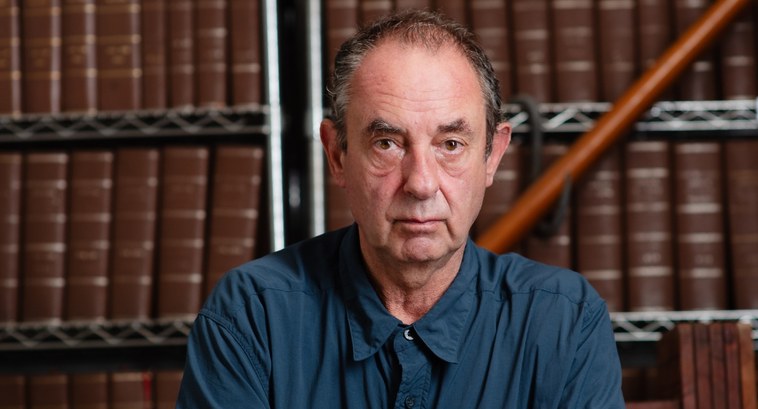 #PraTodosVerem: Na fotografia aparece um homem em primeiro plano, com livros em estantes em segu...