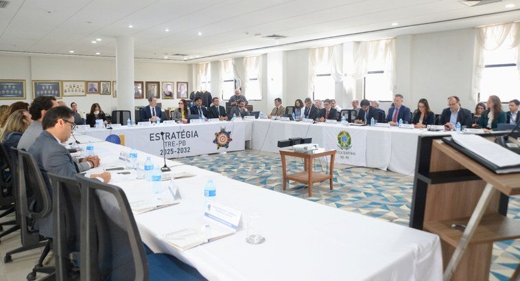 Campina Grande sedia 4ª Reunião de Análise da Estratégia #PraTodosVerem: Na fotografia aparecem diversas pessoas sentadas ao redor de mesas dispostas em ...