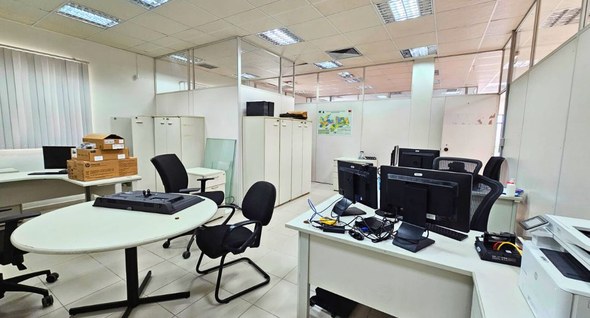 #PraTodosVerem: Na fotografia, o interior de uma sala ampla e ocupada com mesas, cadeiras, compu...