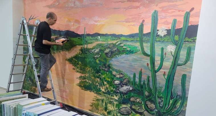 #PraTodosVerem: Na fotografia aparece um artista na escada pintando um mural artístico que repre...