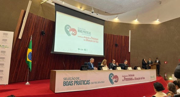 Corregedor do TRE-PB cumpre agenda de integração e premiação em Brasília_ 2 Foto 2: #PraTodosVerem: Na fotografia aparece um palco de auditório com painéis de madeira escur...