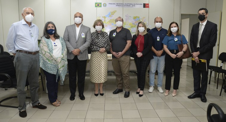 Pessoas perfiladas numa sala de reunião, atrás, na parede, um mapa do Estado da Paraíba.