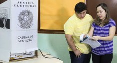 #PraTodosVerem: Na fotografia, um homem e uma mulher em uma sala. À esquerda, uma cabine de vota...