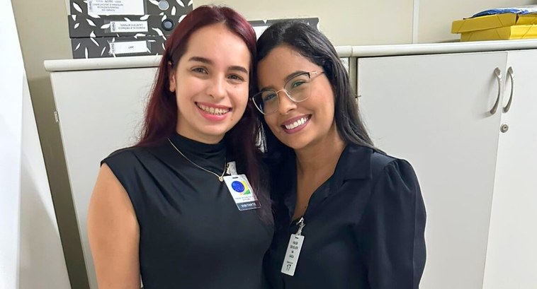 #PraTodosVerem: Na fotografia aparecem duas mulheres, posando, em pé, sorridentes. Em segundo pl...