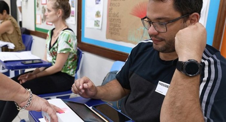 Eleições 2024: Saiba como se candidatar para ser MESÁRIO #PraTodosVerem: Na fotografia aparecem duas mulheres e um homem, sentados em cadeiras, auxiliand...