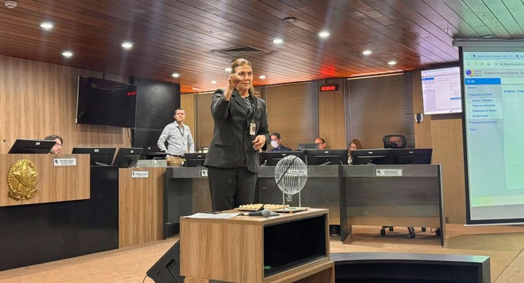 #PraTodosVerem: na fotografia, aparece uma mulher em pé, no centro da sala de sessões, ao lado d...