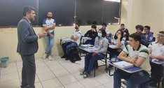 #PraTodosVerem: Na fotografia aparecem dois homens em pé, e diversos alunos, sentados em cadeira...