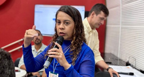 #PraTodosVerem: Na fotografia aparece uma mulher de pé, com blusa azul e microfone, falando para...