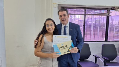 #PraTodosVerem: Na fotografia aparecem uma mulher e um homem, em pé, posando; ambos seguram um d...