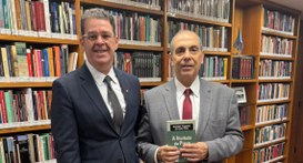 #PraTodosVerem: Na fotografia aparecem dois homens, em pé, posando; um dos homens segura um livr...