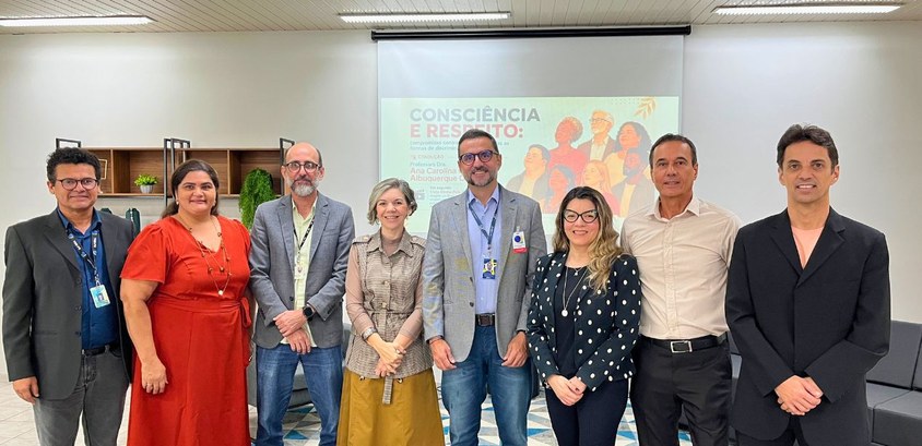 #PraTodosVerem: Na fotografia aparece um grupo de pessoas posando para foto tendo ao fundo a exi...