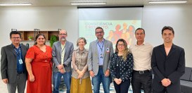 #PraTodosVerem: Na fotografia aparece um grupo de pessoas posando para foto tendo ao fundo a exi...