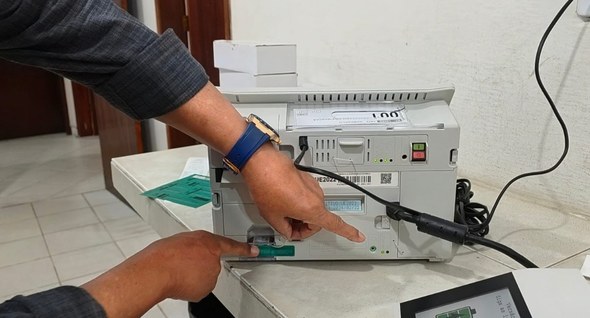 nvi_preparacao_urnas_cabedelo_1 Foto 1: #PraTodosVerem: Na fotografia aparece a mão de uma pessoa, segurando um documento, a fre...