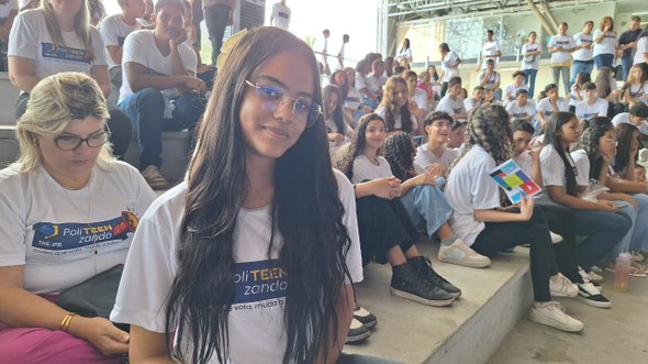 #PraTodosVerem: Na fotografia aparece uma jovem, usando óculos, sorrindo para a câmera. Ela está...