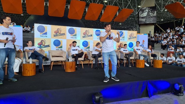 #PraTodosVerem: Na fotografia aparece um auditório com várias pessoas assistindo a um evento. No...