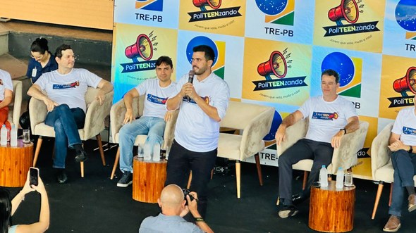 #PraTodosVerem: Na fotografia aparece um palco com cinco homens em um evento. No centro, um home...