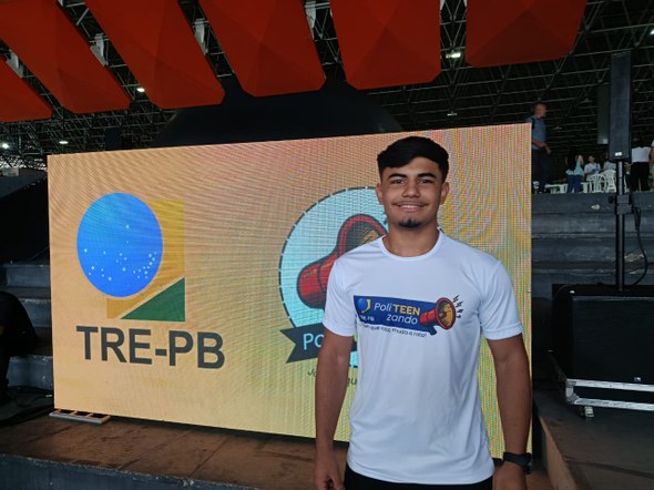 #PraTodosVerem: Na fotografia aparece um jovem, sorrindo e trajando uma camiseta branca. Ele est...