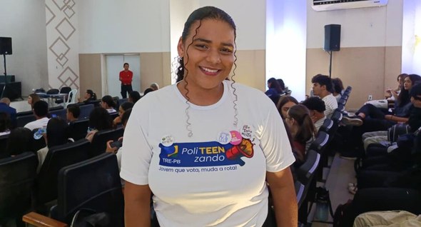 #PraTodosVerem: Na fotografia aparece uma jovem, em primeiro plano, usando uma camiseta branca d...