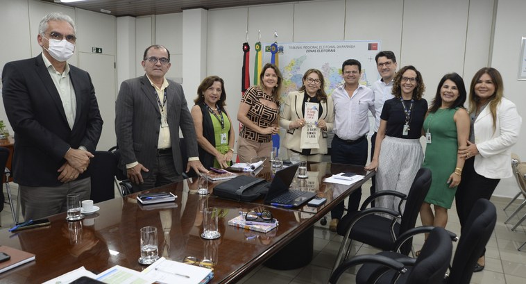 Presidente do TRE-PB é presenteada com livro de servidor da Justiça Eleitoral #PraTodosVerem: Na fotografia aparecem pessoas na Sala da Presidência do TRE-PB
