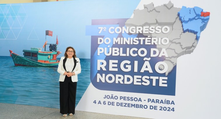 Presidente do TRE-PB participa de evento do Ministério Público #PraTodosVerem: Na fotografia, aparece um mulher em pé, posando, com o banner do evento ao fundo.