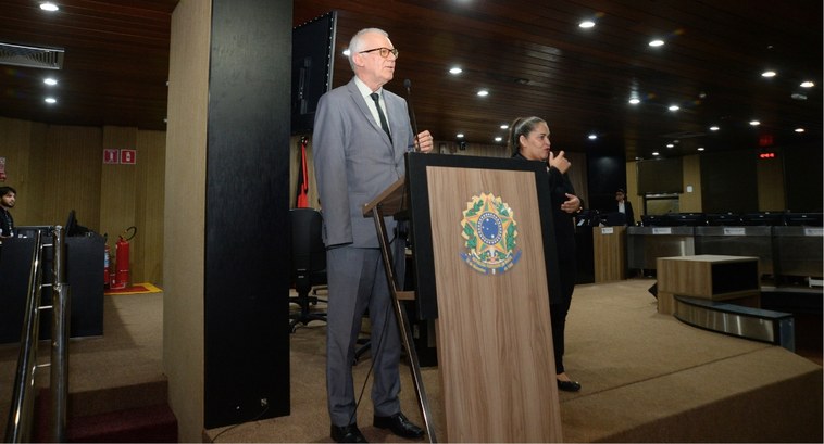 Projeto Cuidar é lançado com a presença do ministro do STJ Sérgio Kukina_capa #PraTodosVerem: Na fotografia, um homem de terno fala ao microfone em um púlpito com o brasão da...
