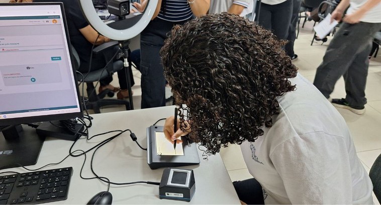 Projeto leva quase 900 jovens da Capital a fazer o título de eleitor_CAPA #PraTodosVerem: Na fotografia aparece uma jovem de cabelos cacheados fazendo o alistamento eleit...