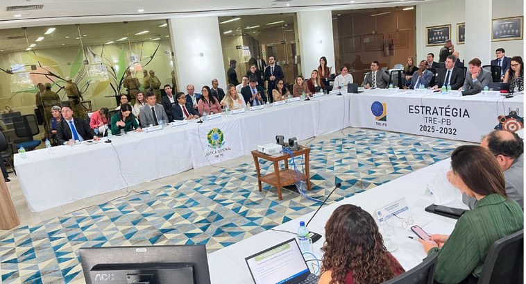 #PraTodosVerem: Na fotografia homens e mulheres sentados em uma mesa,  em que no ângulo principa...