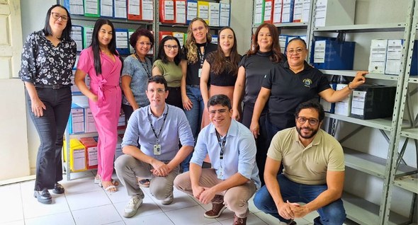 #PraTodosVerem: Na fotografia aparece um grupo de pessoas posando em frente a caixas de document...
