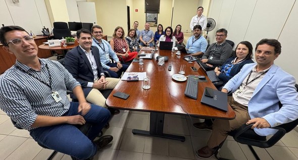 #PraTodosVerem: Na fotografia aparecem pessoas, reunidas em volta de uma mesa de madeira, sentad...