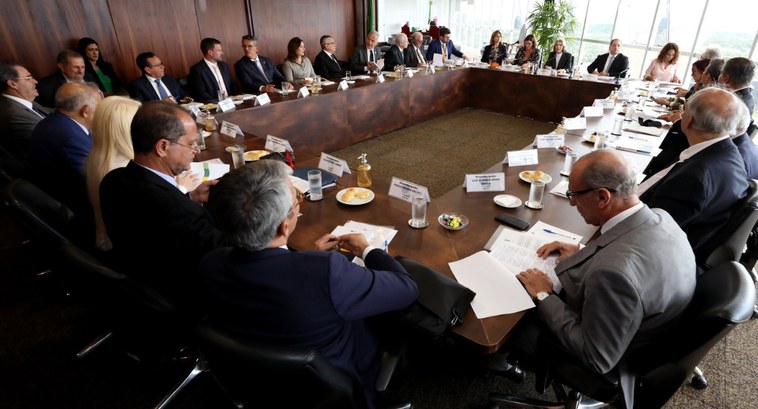 #PraTodosVerem: Na fotografia aparece uma sala de reuniões ampla com autoridades sentadas ao red...