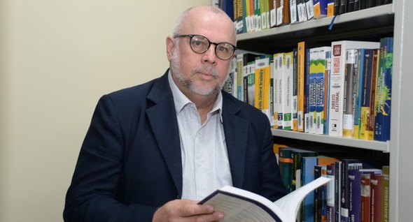#PraTodosVerem: Na fotografia aparece um homem posando, segurando um livro entre as mãos; à dire...