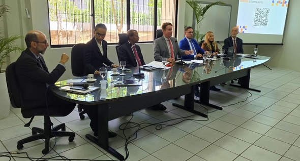 terceira_reuniao_orcamento_cg_1 #PraTodosVerem: Na fotografia interna 1 aparece um grupo de sete pessoas sentadas numa mesa reta...