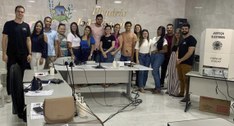 #ParaTodosVerem: Pessoas, homens e mulheres, perfiladas por trás de uma mesa, num local de votação.