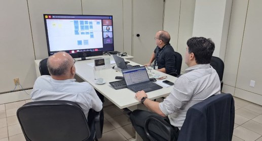 PraTodosVerem: Na imagem pessoas, semtadas à mesa, participando de uma reunião. Também aparece u...