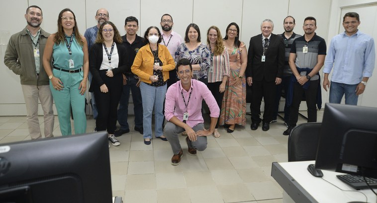 Pessoas perfiladas e uma de cócoras, todas posando para fotografia numa sala de treinamento.