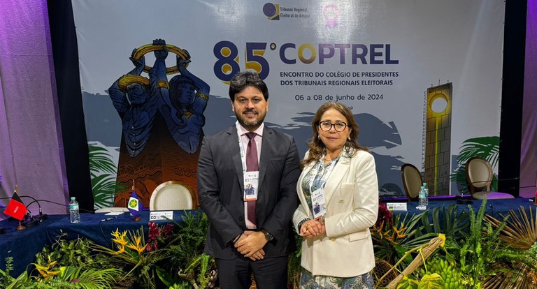 Painel retangular com um homem e uma mulher, ambos de pé, posando para fotografia.