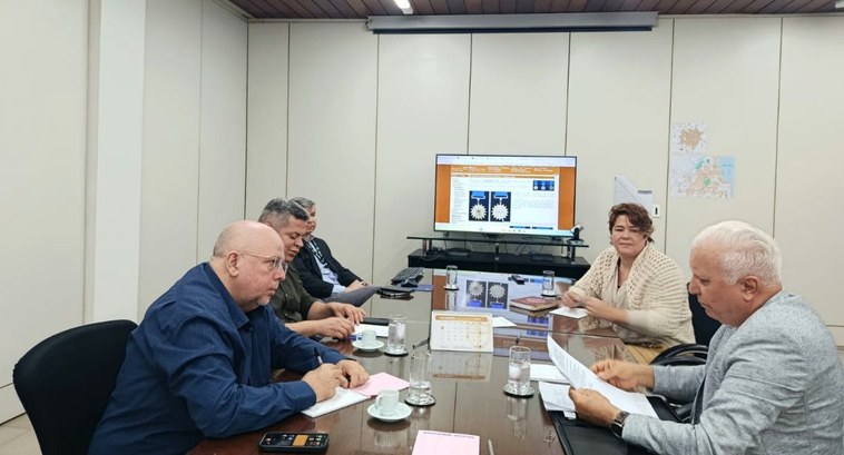 Foto interna. Na fotografia aparecem pessoas em uma sala de reunião, em que aparece uma tela mos...