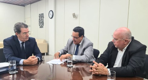 #PraTodosVerem: Ao redor de uma grande mesa de reuniões de vidro, 3 homens participam de uma reu...