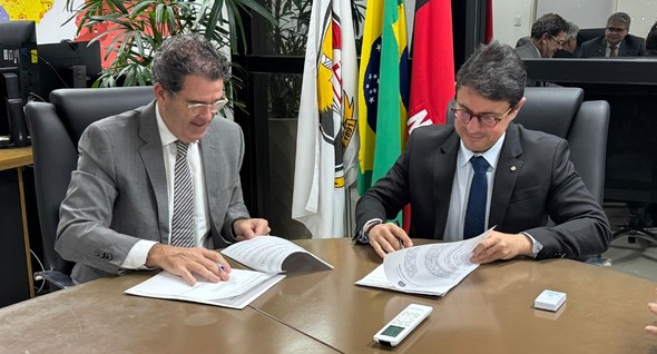 TRE-PB e MPPB assinam termo para viabilizar usina fotovoltaica Foto 1: #PraTodosVerem: Na fotografia, dois homens sentados à mesa, um de frente para o outro, d...
