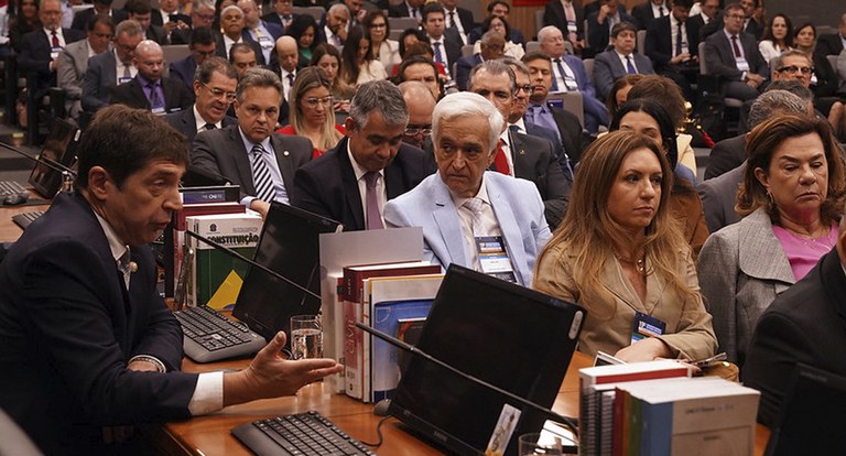 Pessoas assistindo palestra num auditório; em primeiro plano, um homem faz explanação.
