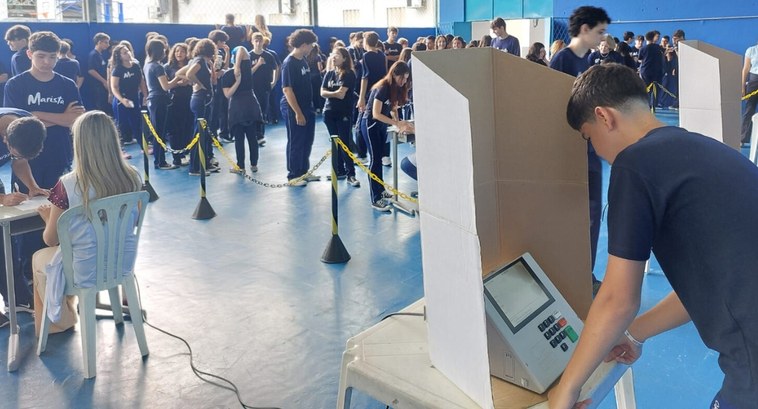 TRE-PB estimula exercício da cidadania e promove a democracia com empréstimos de urnas eletrônicas #PraTodosVerem: Na fotografia aparecem estudantes uniformizados em um ginásio. Eles participam d...