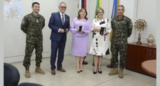 Painel retangular com cinco pessoas de pé, duas mulheres e três homens, posando para fotografia.